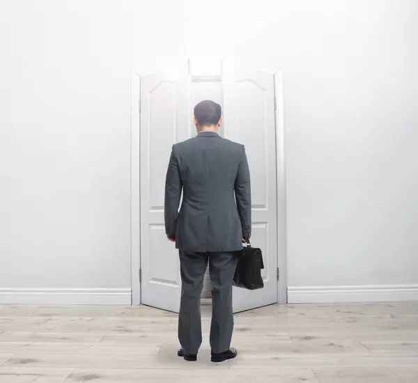 Man with briefcase standing in front of open door, back view