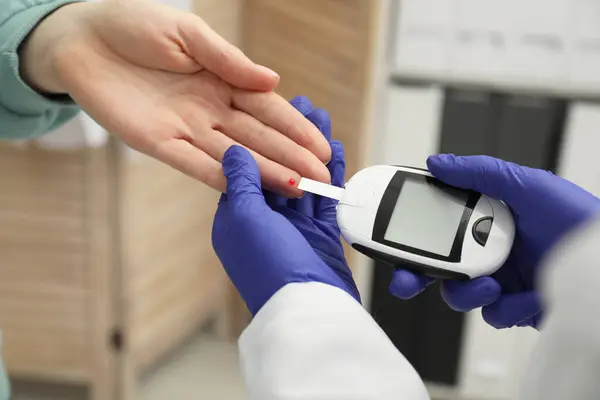 Diabetes. Doctor checking patient\'s blood sugar level with glucometer in clinic, closeup
