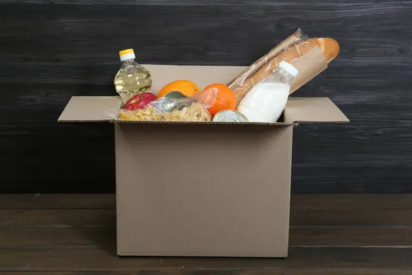 Cardboard box with donation food on wooden table, closeup