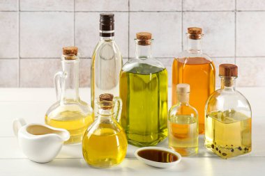 Sebze yağları. Cam şişelerde farklı yağlar ve duvarlara karşı beyaz ahşap masada bulaşık malzemeleri.