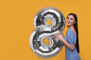 Mutlu Kadınlar Günü. Turuncu arka planda 8 numara şeklinde balon tutan alımlı kadın.