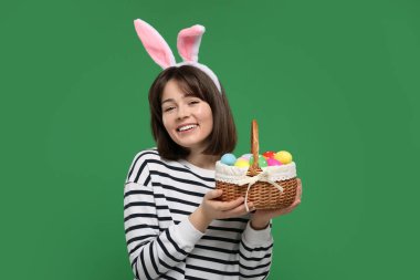 Paskalya kutlaması. Tavşan kulaklı mutlu kadın ve yeşil arka planda boyanmış yumurtalarla dolu sepet.