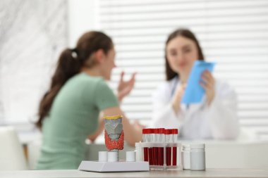 Endocrinologist examining patient at clinic, focus on model of thyroid gland, pills and blood samples in test tubes clipart