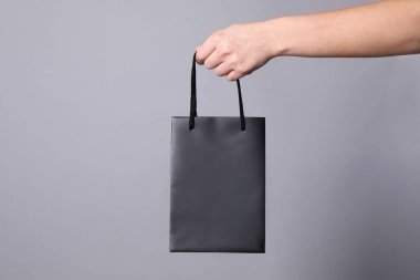 Gri arka planda kağıt alışveriş torbası tutan kadın, yakın plan. Metin için boşluk