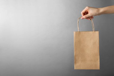 Gri arka planda Kraft kağıt çantası tutan bir kadın, mesaj için yeri olan yakın plan. Tasarım için model