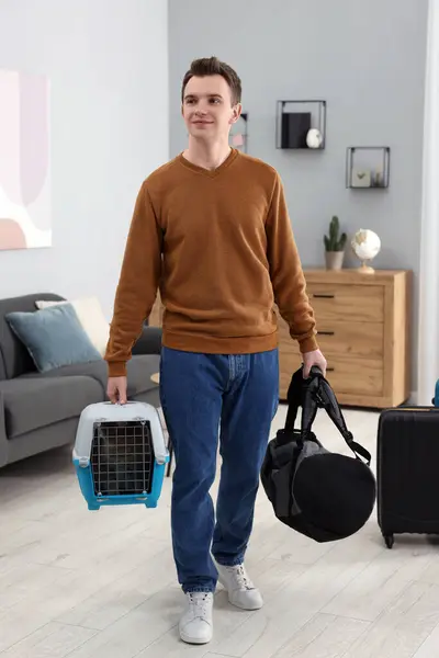 Travel with pet. Man holding carrier with cute cat and bag at home