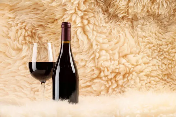 Stylish presentation of delicious red wine in bottle and glass on fluffy surface. Space for text