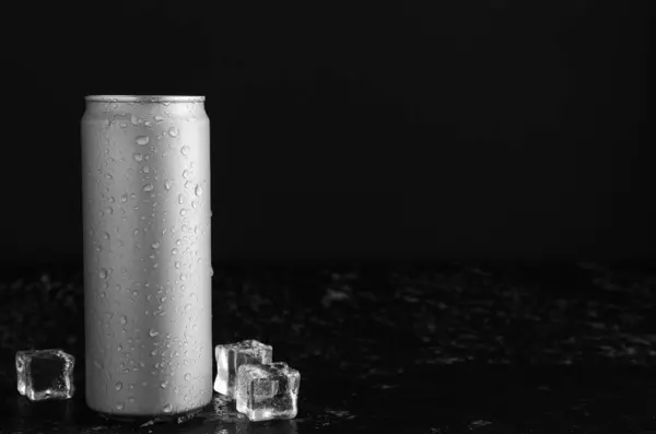 Energy drink in wet can and ice cubes on black textured table, space for text