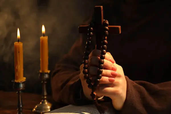 Woman praying at table with burning candles and cross, closeup