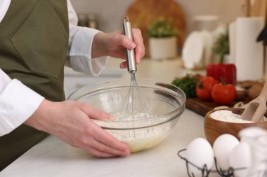 Işık masasında çırpıcıyla hamur yapan kadın, yakın plan.