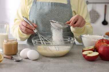 Kapalı mekandaki gri masada un ellerken yumurta çırpan kadın, yakın plan.