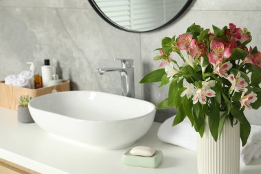 İçinde güzel Alstroemeria çiçekleri ve banyo lavabosunun yanında tuvalet malzemeleri olan vazo.