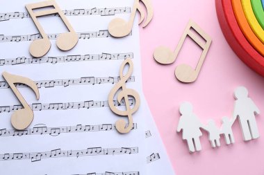 Bebek şarkıları. Müzik kağıtları, aile figürleri, ahşap notalar ve pembe arka planda oyuncak gökkuşağı.