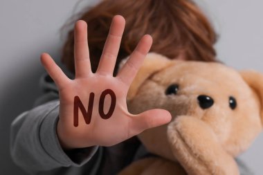 Çocuk istismarı. Oyuncaklı çocuk gri duvarın yanında dur hareketi yapıyor, seçici odaklanma. Elinde bir şey yazmıyor.