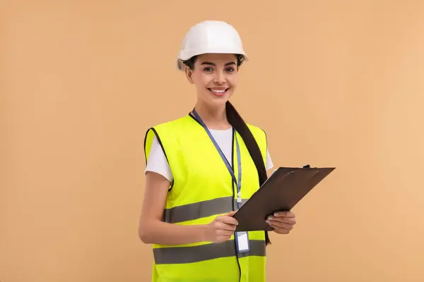 Engineer in hard hat holding clipboard on beige background
