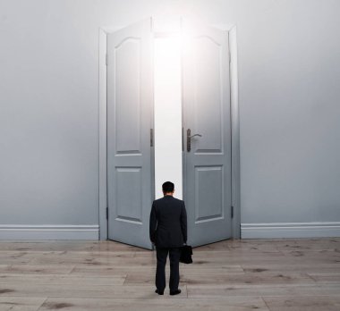 Evrak çantalı bir adam açık kapının önünde dikiliyor.