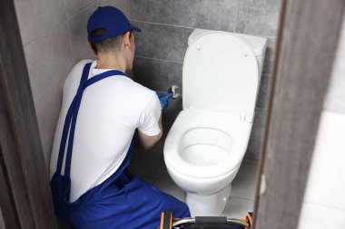Su dolabındaki klozeti tamir eden anahtarı olan bir tesisatçı.