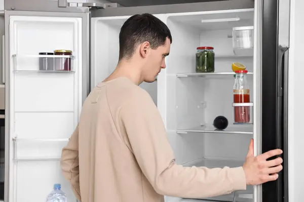 Man near empty refrigerator in kitchen at home