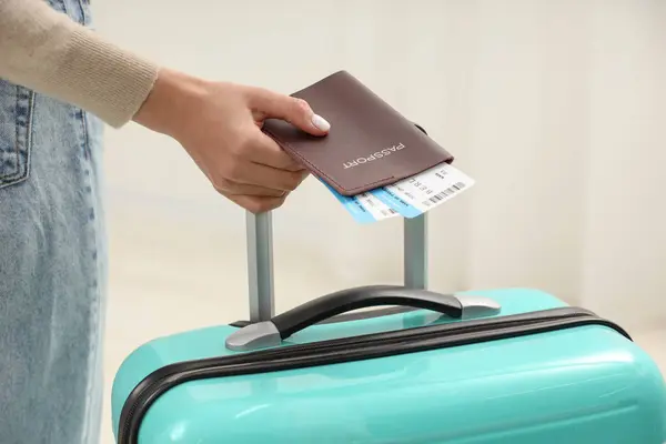 Woman with suitcase, passport and tickets on blurred background, closeup