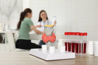 Endocrinologist examining patient at clinic, focus on model of thyroid gland and blood samples in test tubes clipart