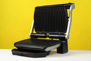 Beyaz ahşap masada elektrikli ızgara, sarı arka planda, yakın plan. Yemek pişirme aygıtı