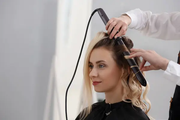 Hair styling. Hairdresser curling woman's hair in salon, closeup. Space for text
