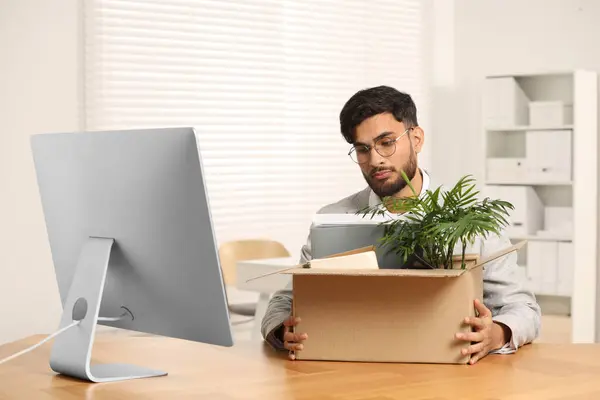 Unemployment problem. Frustrated man with box of personal belongings at desk in office