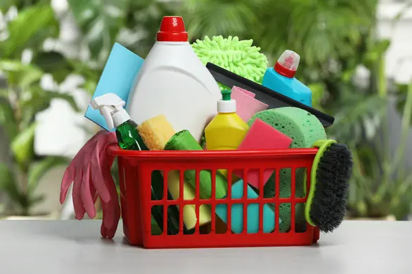 Different cleaning products in plastic basket on light grey table indoors