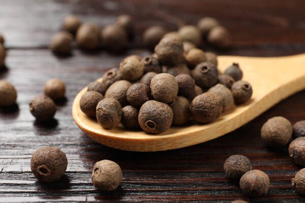 Dry allspice berries (Jamaica pepper) and spoon on wooden table, closeup