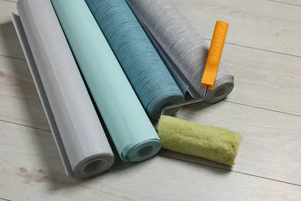 Different wallpaper rolls and roller on floor