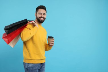 Kağıt alışveriş poşetleriyle gülümseyen ve açık mavi arka planda kahve ısmarlayan adam. Metin için boşluk
