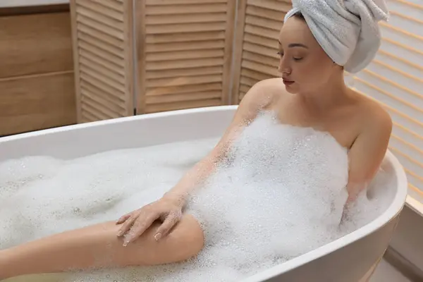 Beautiful woman taking bath with foam in tub indoors, space for text