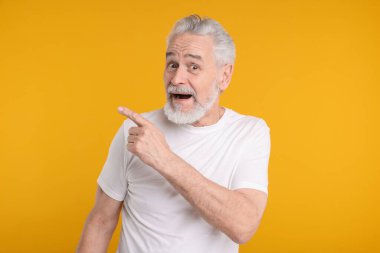 Şaşkın kıdemli adam sarı arka plandaki bir şeyi işaret ediyor.