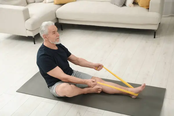 Senior man doing exercise with fitness elastic band on mat at home