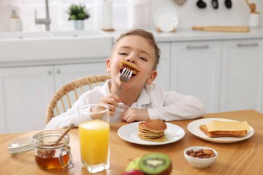 Kahvaltı vakti geldi. Mutfaktaki masada krep yiyen sevimli küçük çocuk.