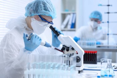 Laboratuvarda mikroskopla çalışırken cam parçasına kan damlatan bir bilim adamı.