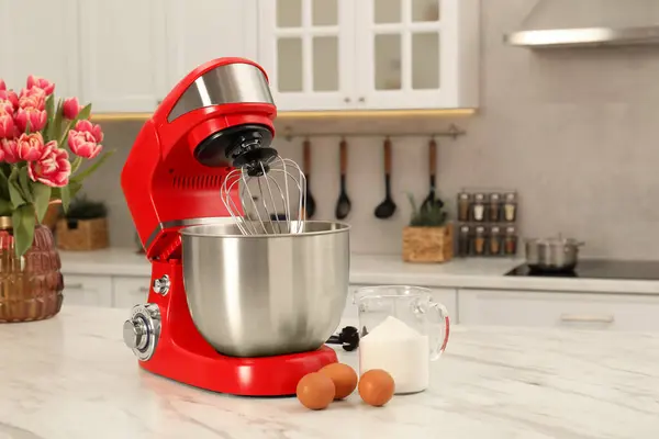 Modern red stand mixer, eggs and container with flour on white marble table in kitchen
