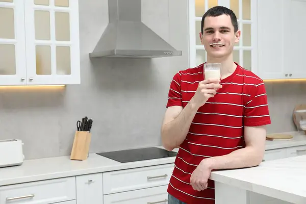 Happy man with milk mustache holding glass of tasty dairy drink in kitchen