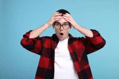 Açık mavi arka planda gözlüklü şaşırmış adam.