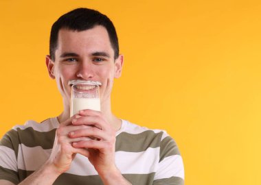 Süt ürünlerinden sonra bırakılan süt bıyığı. Turuncu arka planda süt içen adam, metin için boşluk