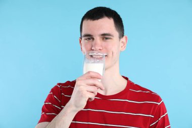 Süt ürünlerinden sonra bırakılan süt bıyığı. Açık mavi arka planda süt içen adam