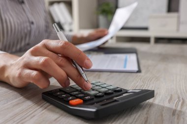Ofisteki açık tahta masada hesap makinesi kullanan kadın, yakın plan.