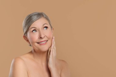 Bej arka planda sağlıklı cildi olan güzel olgun bir kadın.