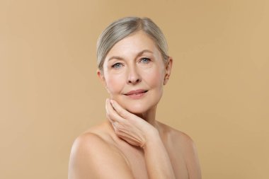 Bej arka planda sağlıklı ciltli güzel olgun bir kadın.