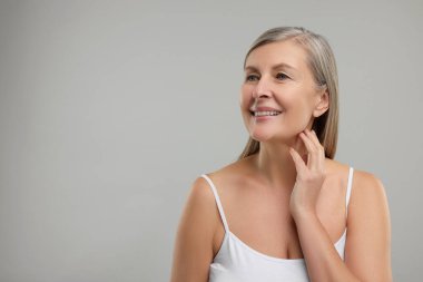 Gri arka planda boynuna dokunan güzel bir kadın, mesaj için boşluk