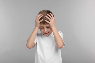 Küçük çocuk gri arka plan üzerinde baş ağrısı muzdarip