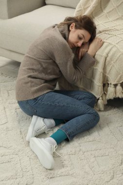 Üzgün genç kadın evde yerde oturuyor.