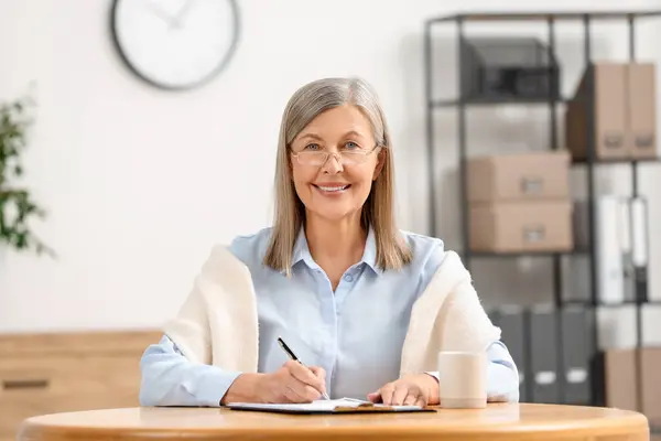 Smiling senior woman signing Last Will and Testament at table indoors
