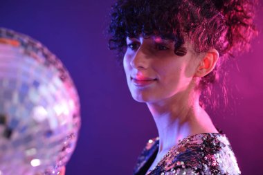 Disko topuyla güzel genç bir kadın neon ışıklarıyla arka planda poz veriyor.