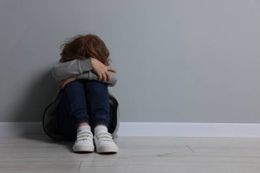 Çocuk istismarı. Üzgün çocuk gri duvarın yanında oturuyor, mesaj için yer var.